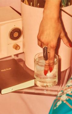 a woman's hand holding a pen over a glass with water