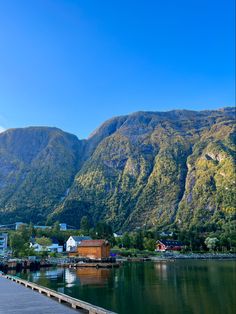 there is a boat dock on the water next to some mountains and houses in the distance