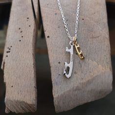 a silver and gold necklace with the letter j on it sitting on a piece of wood