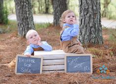 two young children sitting on top of a crate in the woods with chalkboard signs