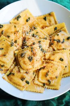 a white plate topped with pasta covered in cheese and herbs on top of a green table cloth