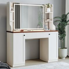 a white dressing table with a mirror and lights on it in a room next to a potted plant