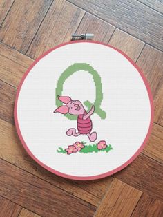 a cross stitch pattern with the letter q in pink and green on a wooden floor