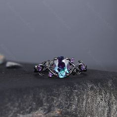 a ring with purple and blue stones on it sitting on top of a black rock