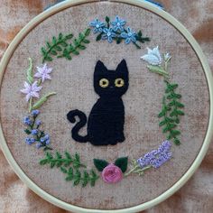 a black cat sitting on top of a wooden hoop with flowers and leaves around it