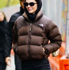 a woman is walking down the street wearing a brown jacket and black leggings