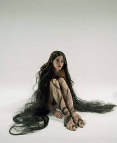 a woman sitting on the ground with long hair in front of her face and legs