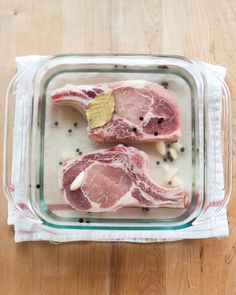 two raw meats in a glass dish on a wooden table with spices and seasonings