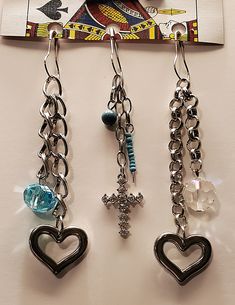 three pairs of heart shaped earrings hanging from hooks on a table next to a card board