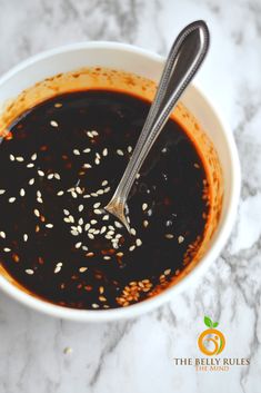 a bowl filled with sesame seeds and sauce on top of a marble countertop next to a spoon