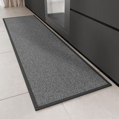 a black door mat on the floor in front of a white tiled wall and window