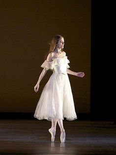 a woman in a white dress standing on a stage with her arms out and legs spread wide