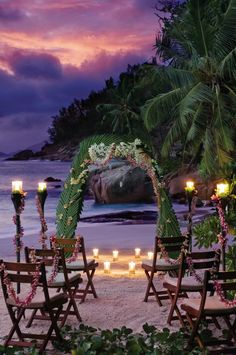 an outdoor ceremony set up with candles and flowers on the beach at dusk, surrounded by palm trees