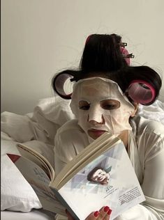 a woman laying in bed reading a book with her face painted like a monkey on top of it