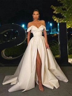 a woman standing in front of a sign wearing a white dress with high slits