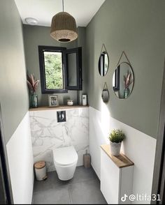 a white toilet sitting next to a window in a bathroom under a light fixture with three mirrors on the wall