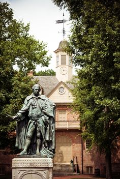 a statue in front of a building with a clock on it's tower and trees