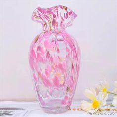 a pink glass vase sitting on top of a table next to white and yellow flowers