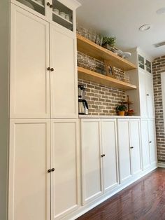 a kitchen with white cabinets and brick wall in the backround, along with hardwood flooring