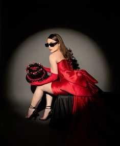 a woman in a red dress sitting on a chair with a black hat and sunglasses