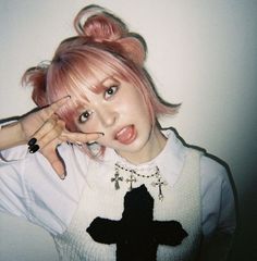 a woman with pink hair and piercings holding her hand up to her face while standing in front of a white wall