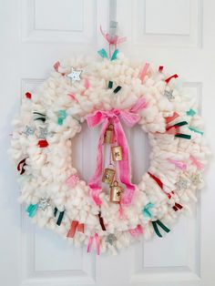 a white wreath with pink ribbon and bells hanging on the front door to welcome guests