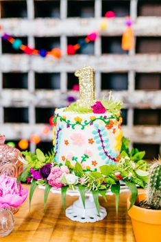 a colorful birthday cake sitting on top of a wooden table next to a cactus plant