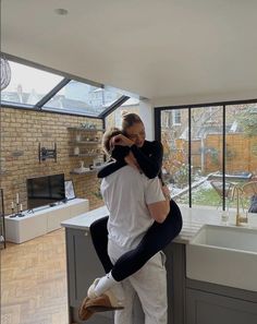 a man holding a woman in his arms while standing next to a kitchen counter top