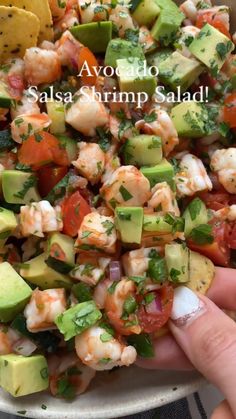 someone is holding up a salad with shrimp, avocado and tomatoes in it