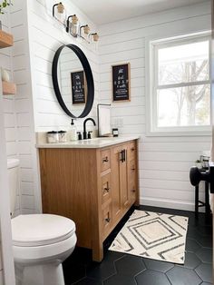 a white toilet sitting next to a bathroom sink under a mirror on top of a wooden cabinet