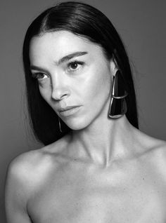 a black and white photo of a shirtless woman with large hoop earrings on her ear