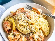 a white bowl filled with pasta and shrimp next to a slice of lemon wedged bread