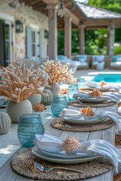 the table is set with plates and place settings for an outdoor dining area by the pool