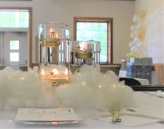 a table topped with candles and white fluffy clouds on top of a glass vase filled with water