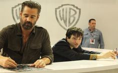 two men sitting at a table signing autographs in front of the people behind them