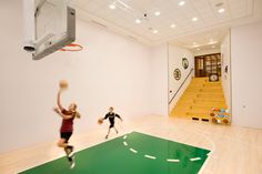 two people are playing basketball in an indoor gym with stairs leading up to the second floor