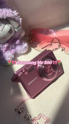 a purple camera sitting on top of a table next to a stuffed animal