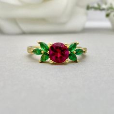 This beautiful ring is made from genuine 925 sterling silver with Yellow Gold plating. Ring details- -The Main stone is a round cut 6mm Lab Created Ruby Stone -Side stones are 4mm by 2mm Lab Emerald Marquise and 1mm Round simulated diamonds -Ring is casted in solid 925 sterling silver with Yellow Gold plating ( Rose gold and White Rhodium plated also available, please check the drop down menu for more options) -The Total face height of the ring measures 7mms and the band width measures 1.5mms -E Fine Jewelry May Birthstone Flower Ring, Emerald Birthstone Cluster Ring, Fine Jewelry Round Flower Ring With May Birthstone, Green Birthstone Flower Ring, Green Flower Ring With Birthstone, Round Ruby Flower Promise Ring, Round Gemstone Flower Promise Ring, Green Ruby Ring Jewelry, Fine Jewelry Green Ruby Ring