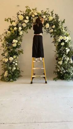 a woman standing on a ladder in front of a floral arch