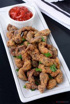 a white plate topped with fried meat next to a small bowl of ketchup