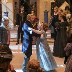 a man and woman dancing in front of an audience at a costume ball with other people standing around