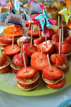 some strawberries are sitting on top of small sandwiches with toothpicks sticking out of them