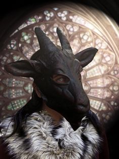 a woman wearing a goat mask in front of a stained glass window with an animal's head on it