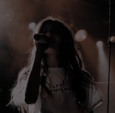 a woman standing in front of a microphone with her hand to her face while wearing a white t - shirt