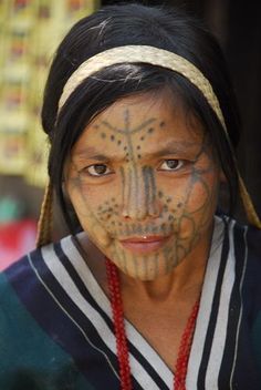 a woman with painted face and headdress in native american style clothing, looking at the camera