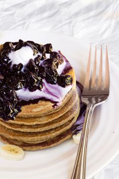 a stack of pancakes topped with blueberries and whipped cream on a white plate next to a fork