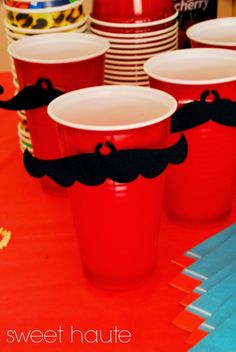 red plastic cups with mustaches on them are sitting on a table in front of paper plates