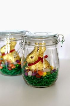 two glass jars filled with candy and gold bunny figurines on top of grass