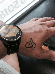 a man's wrist with a small dog tattoo on the left hand and a watch on the right