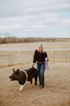 a woman walking her dog on a leash in an open field with a fence behind her